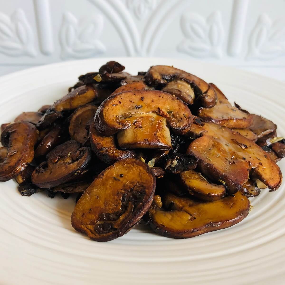 Caramelized mushrooms on a plate against a white tile background.