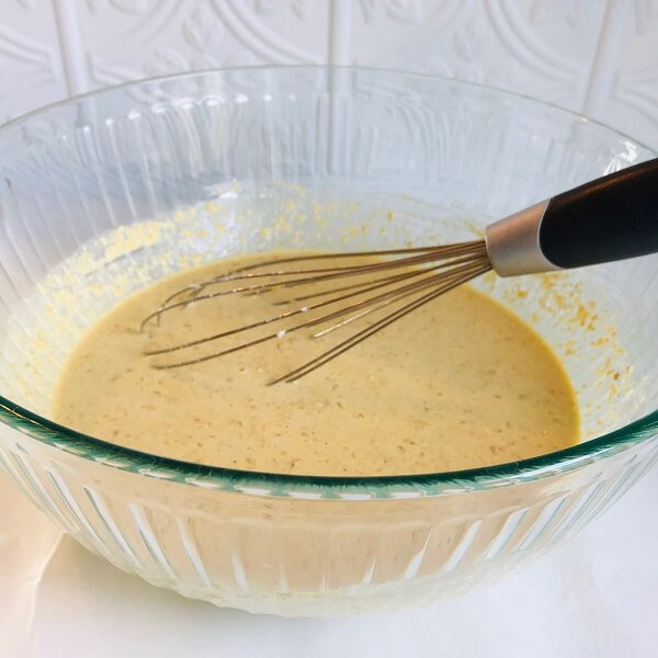 A glass bowl of pancake batter with a whisk.