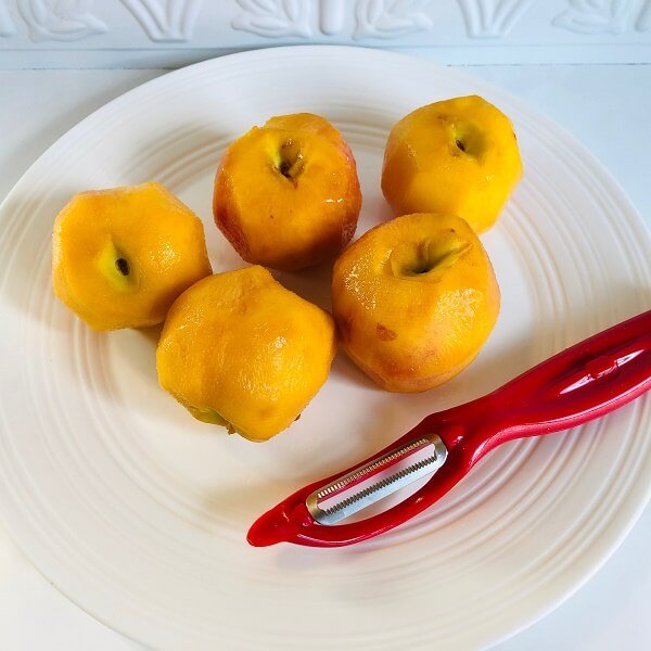 Five peeled peaches next to a red vegetable peeler.