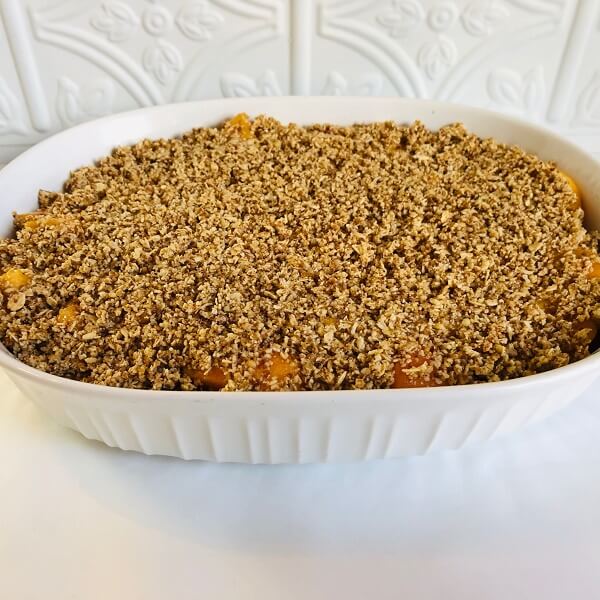 Raw peach crisp in a white casserole dish.