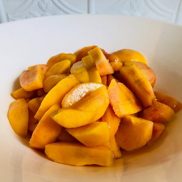 Sliced peaches in a white bowl.