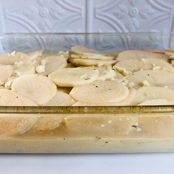 Raw sliced potatoes in a glass baking dish.