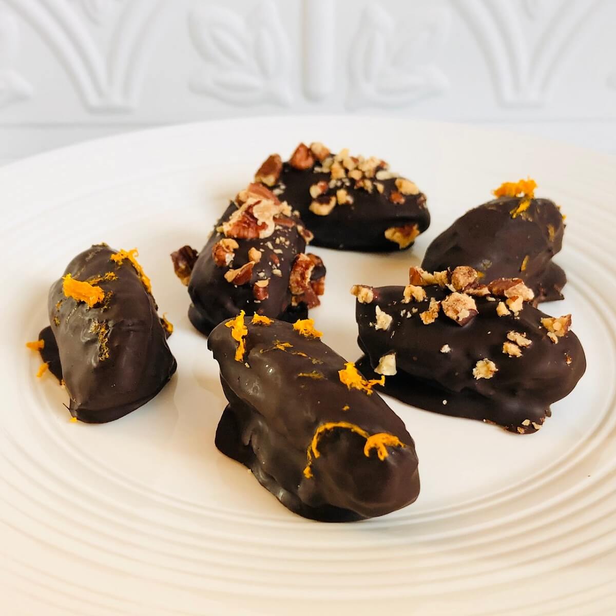 Chocolate covered dates on a white plate.