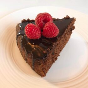 A slice of buckwheat cake with three raspberries on top.