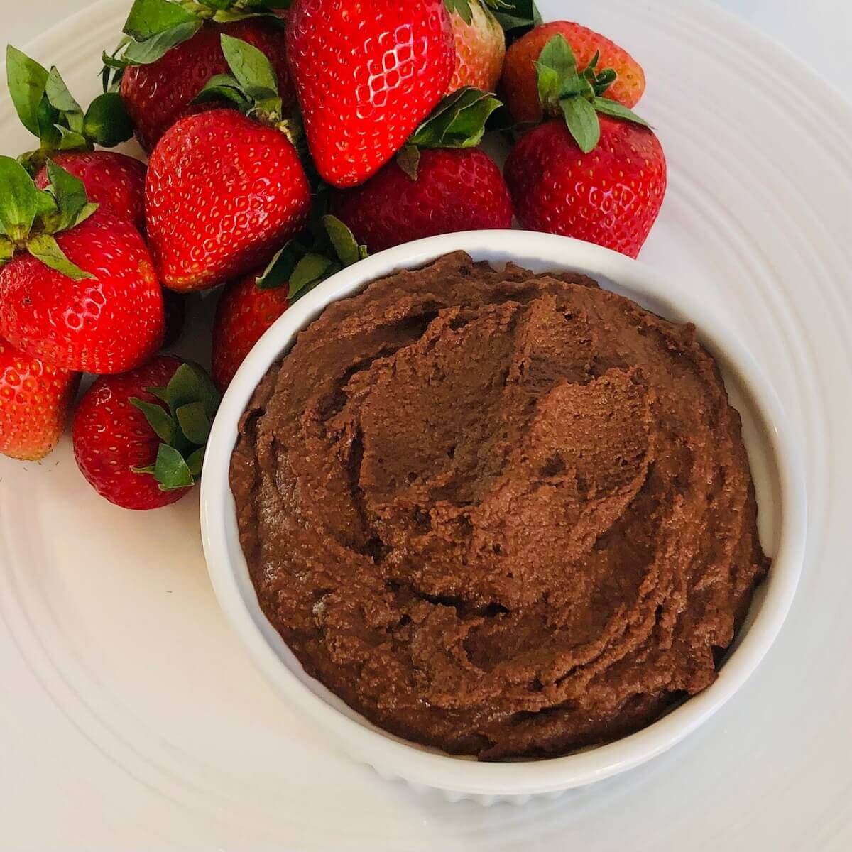 A bowl of dark chocolate hummus next to a pile of strawberries.