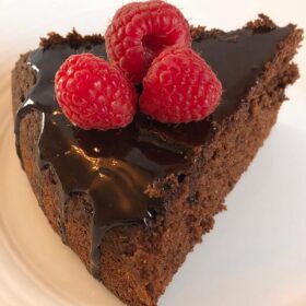 A slice of cake with chocolate glaze and raspberries on top.