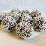Nine chocolate coconut date balls on a white plate.
