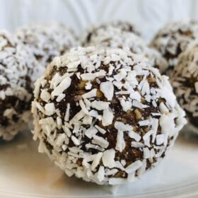 Coconut covered date balls displayed on a white plate.