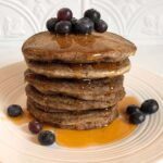 A stack of vegan buckwheat pancakes dripping with maple syrup.