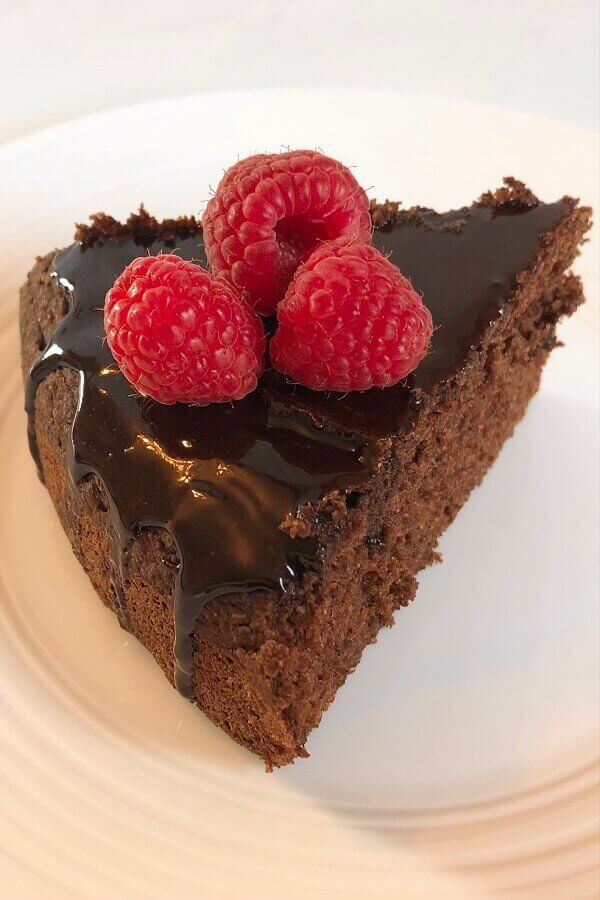 A slice of cake on a plate with raspberries on top.