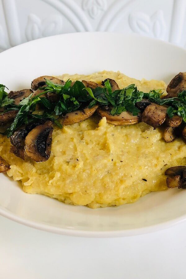 A bowl of polenta with mushrooms and herbs sprinkled on top.