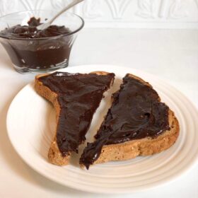 A glass dish full of nut free chocolate spread next to some toast.