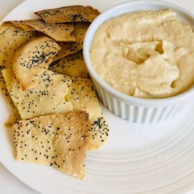 Crackers on a plate next to a dish of hummus.