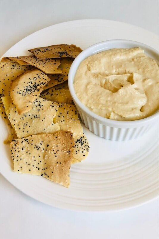 Crackers and hummus on a white plate.