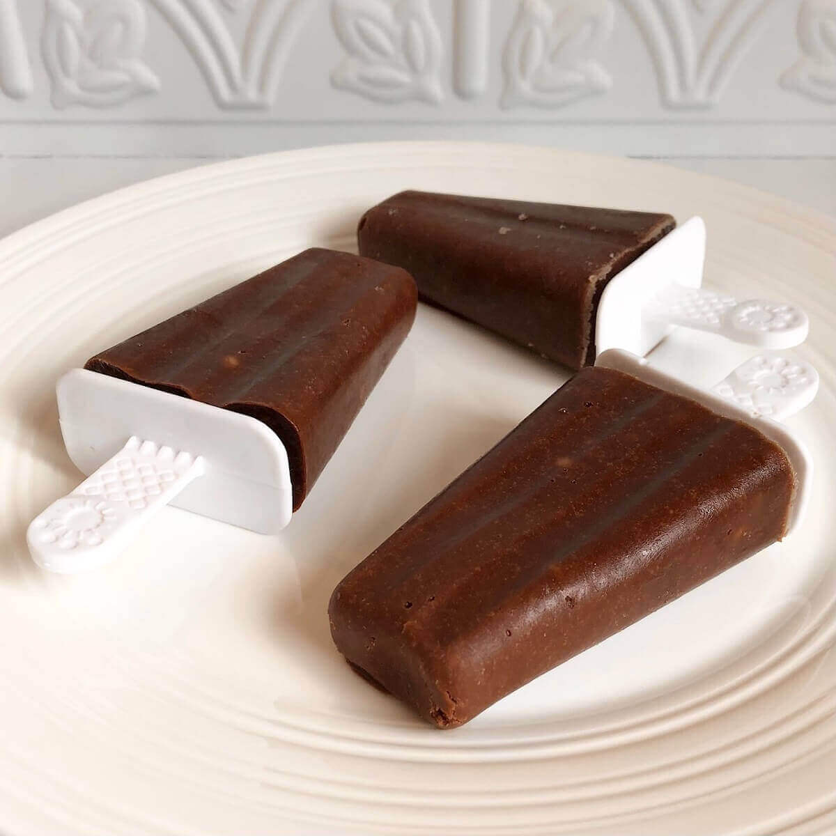 Three banana chocolate popsicles on a plate.