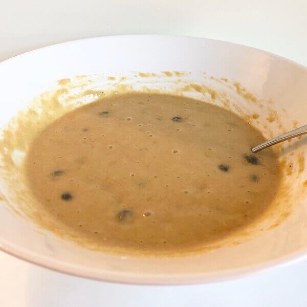 Muffin batter in a large white bowl with a spoon.