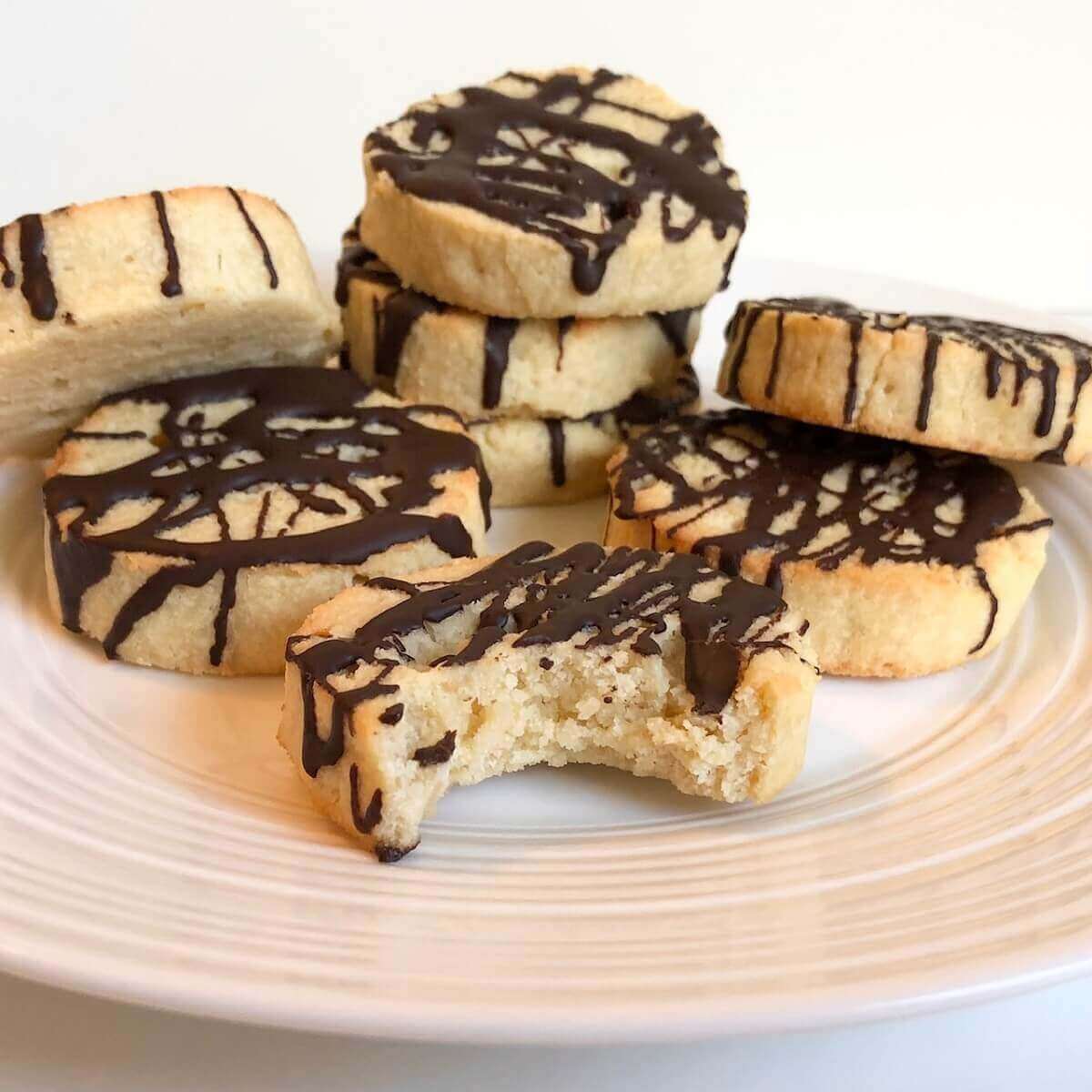 A pile of coconut oil cookies displayed on a white plate with a bite missing from one of them.