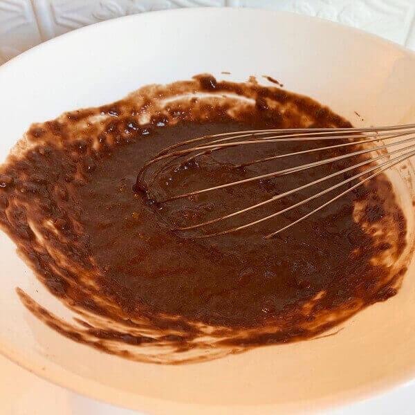 A bowl of brown batter with a whisk.
