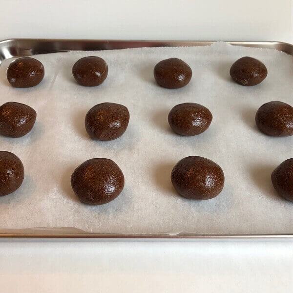 Balls of cookie dough on a sheet pan.