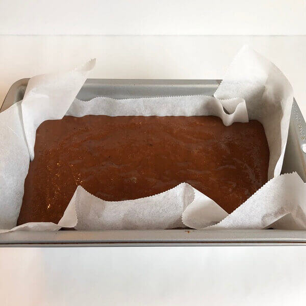 Raw cake batter in a parchment paper lined loaf pan.