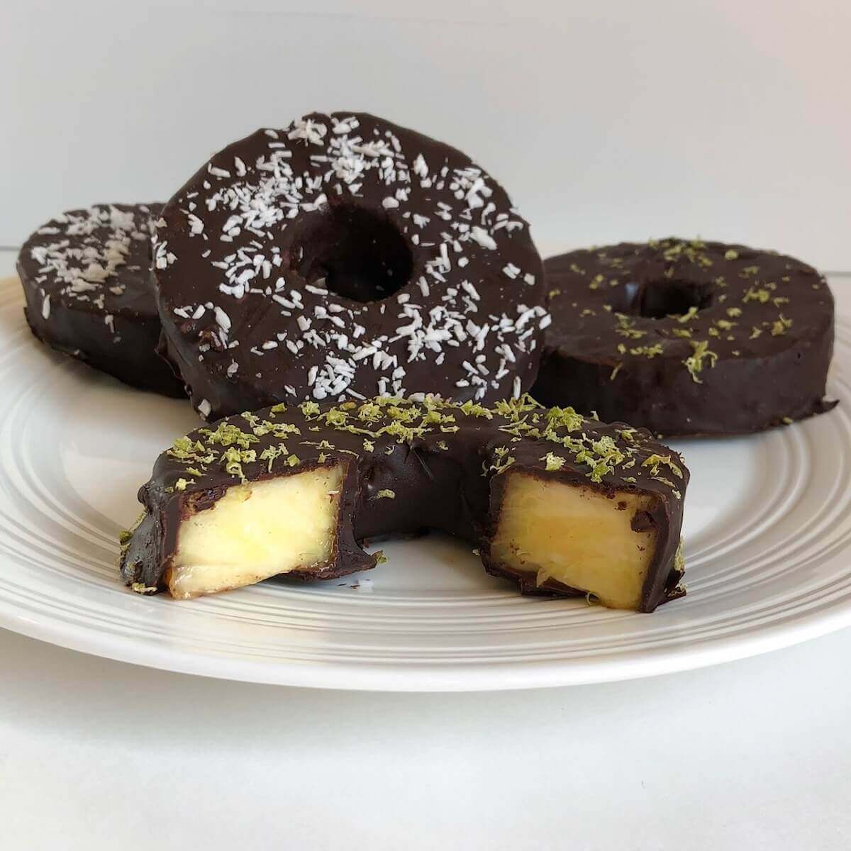 Four chocolate covered pineapple rings on a white plate.