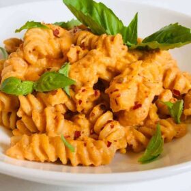 Pasta in a white bowl with fresh basil on top.