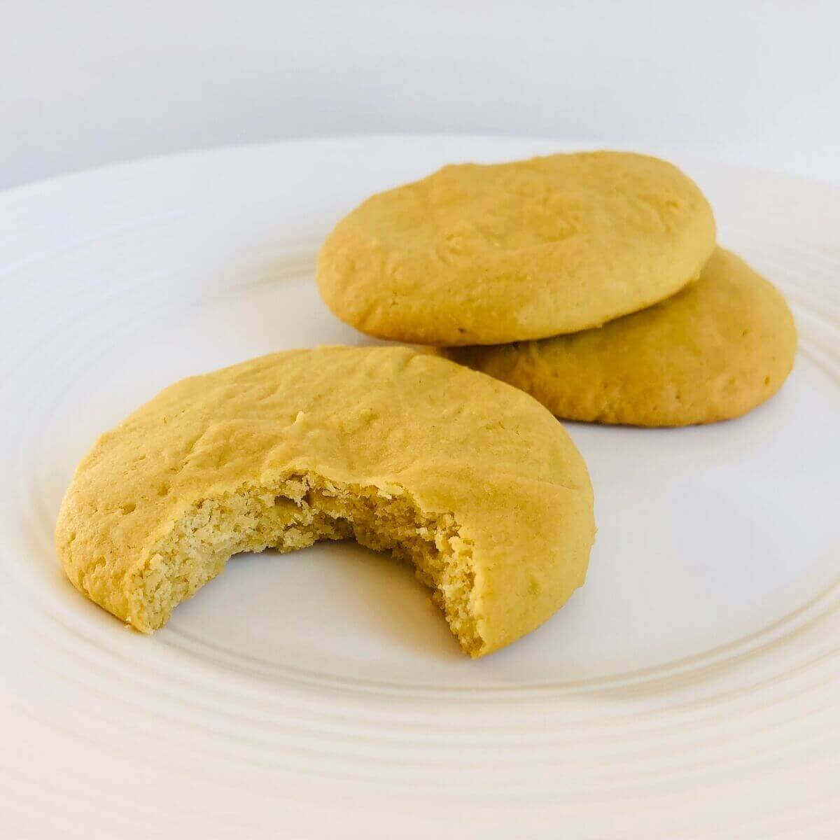 Three corn flour cookies on a plate with a bite missing from one.