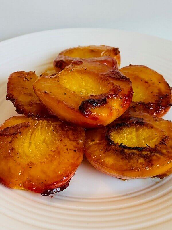 Six cooked peach halves on a white plate.