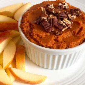 Pumpkin hummus in a ramekin next to apple slices.