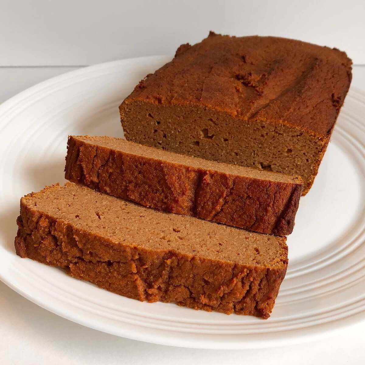 Pumpkin bread loaf and two slices on a white plate.