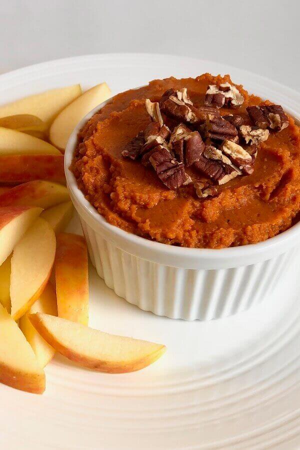 Hummus in a dish next to some apple slices.