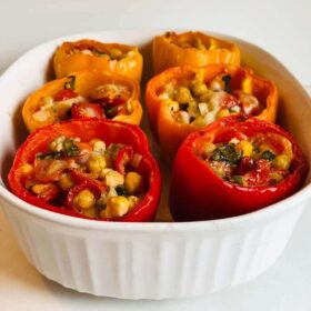 Six cooked chickpea stuffed peppers in a casserole dish.
