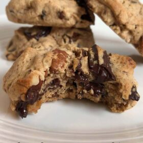 Four cookies on a plate with a bit taken out of one.