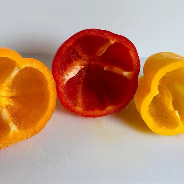 Cross section of three bell peppers on a cutting board.