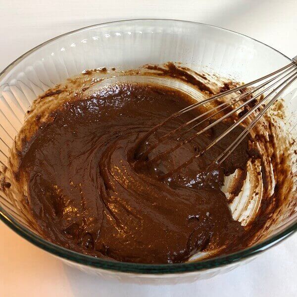 Bread dough being mixed with a whisk in a glass bowl.