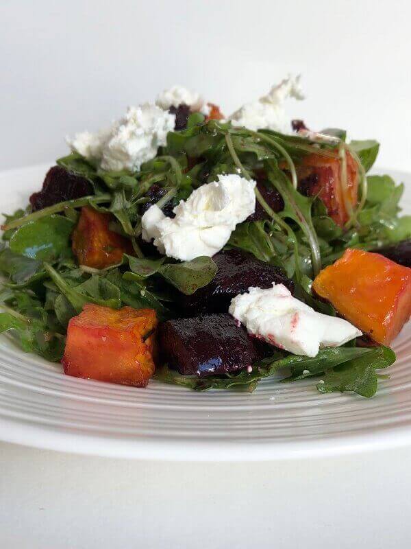 A salad of greens and root vegetables with goat cheese dabbed on top.