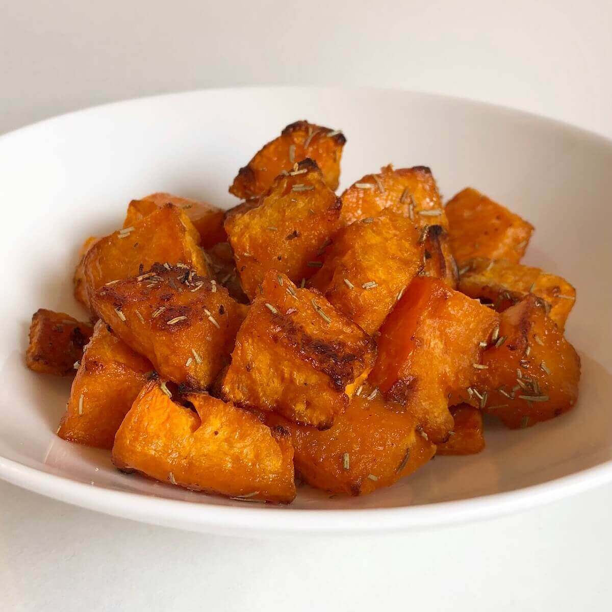 A bowl of roasted butternut squash with rosemary.