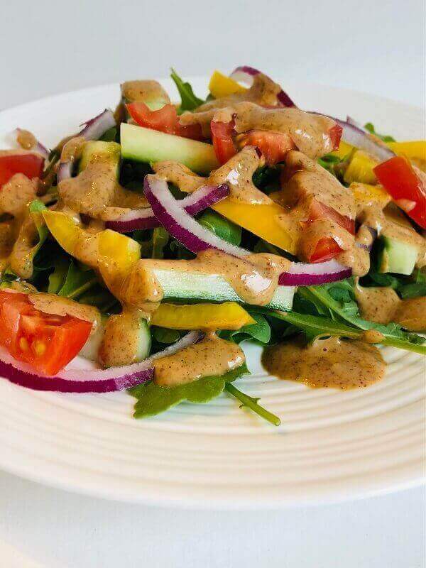 A plate of salad with almond butter dressing drizzled on top.