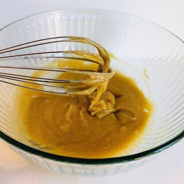 Cookie dough batter dripping off a whisk into a bowl.