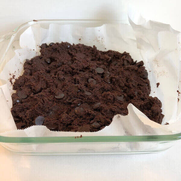 Raw brownie batter in a parchment paper lined baking dish.