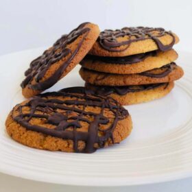 Six vegan olive oil cookies stacked on a white plate.