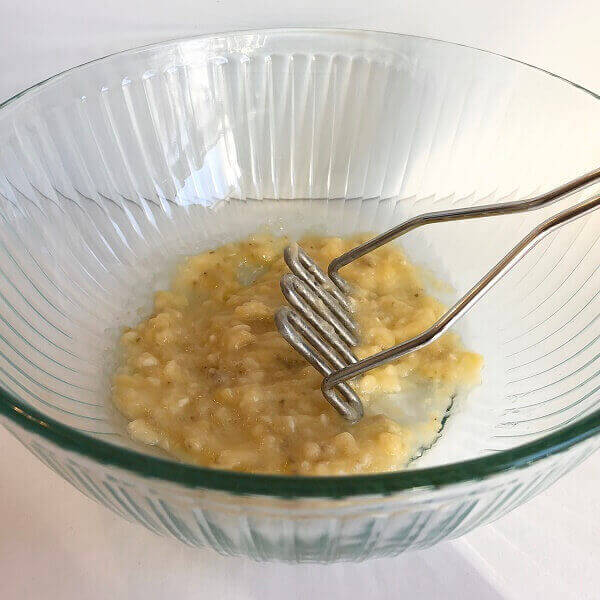 Bananas being mashed in a glass bowl.