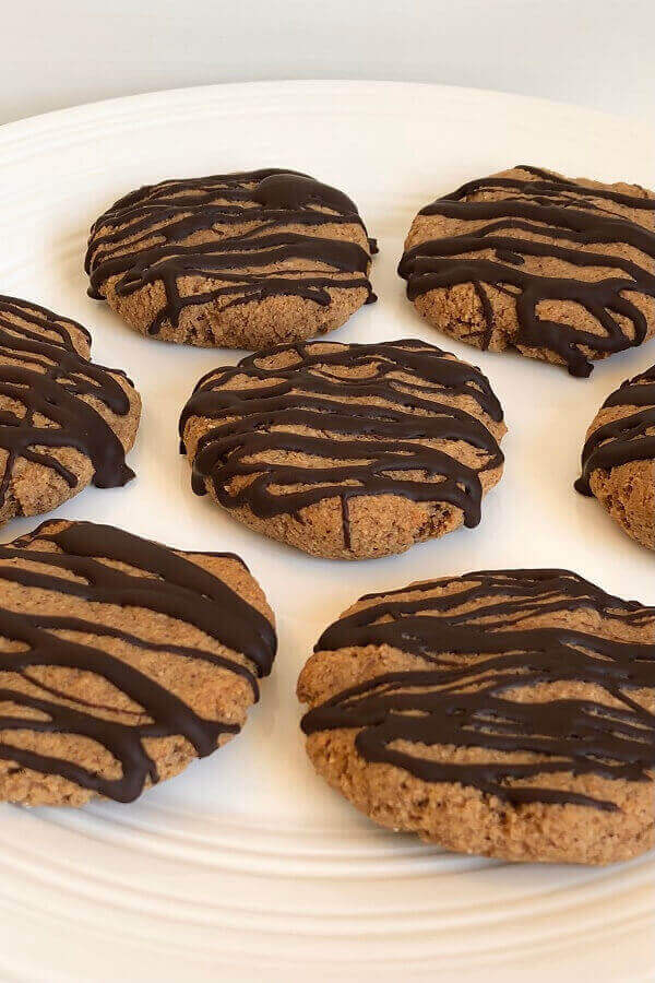 Cookies drizzled with dark chocolate on a white plate.