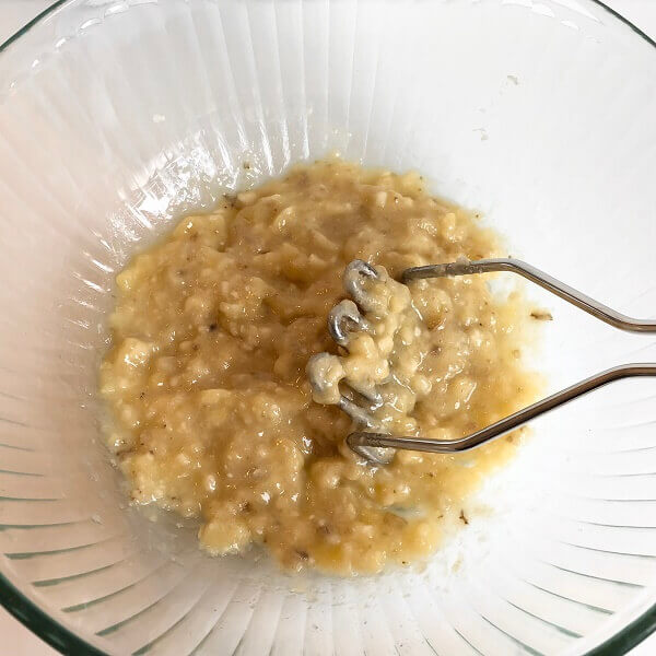 Bananas being mashed by a potato masher.