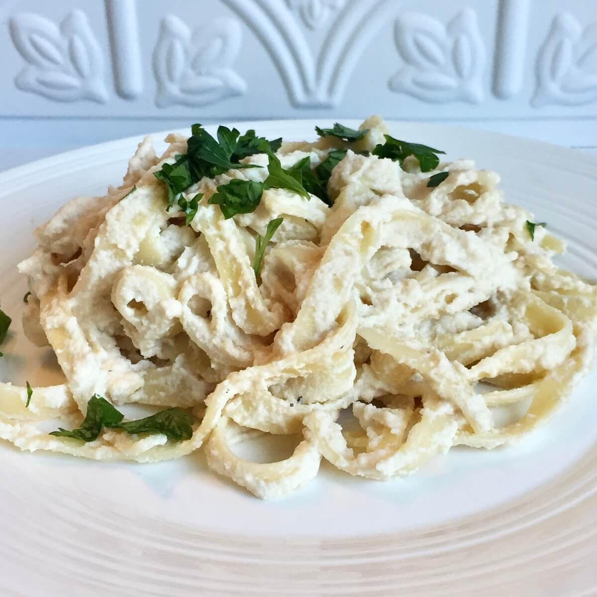 Noodles smothered in a creamy cashew pasta sauce on a white plate.