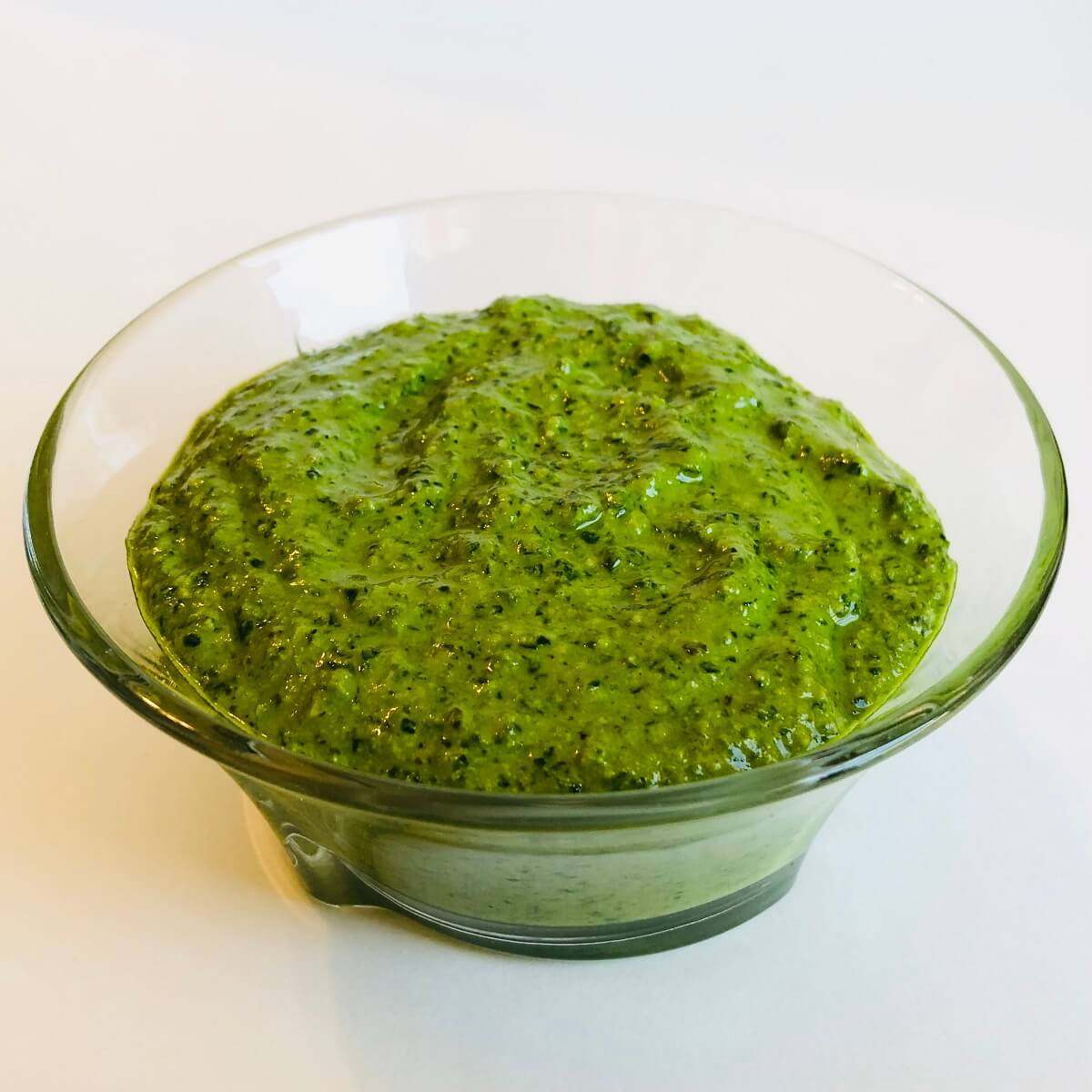 A glass bowl of parsley pesto sauce.