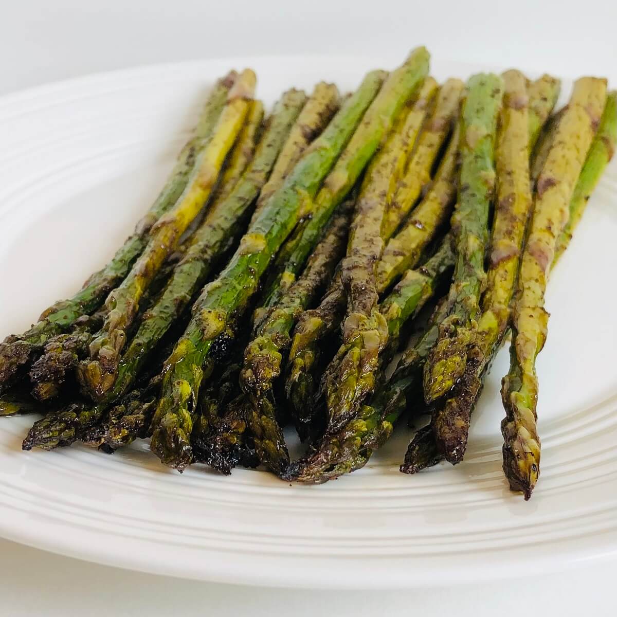 Balsamic roasted asparagus spears on a white plate.