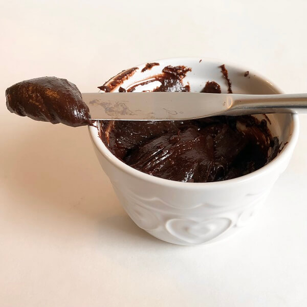 A blob of frosting on a butter knife resting on top of a dish.