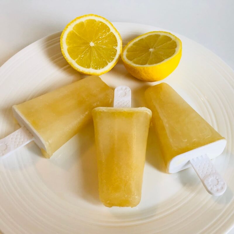 Three popsicles on a plate with a lemon sliced in half.