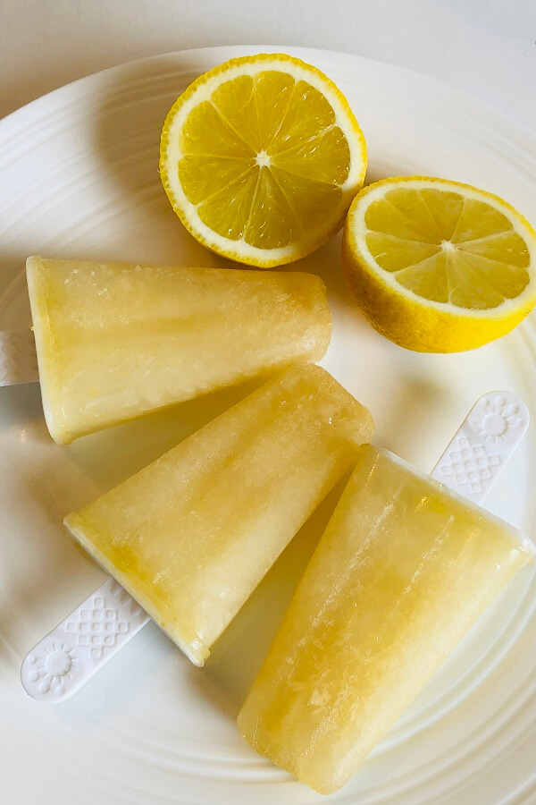 Popsicles and lemons on a white plate.